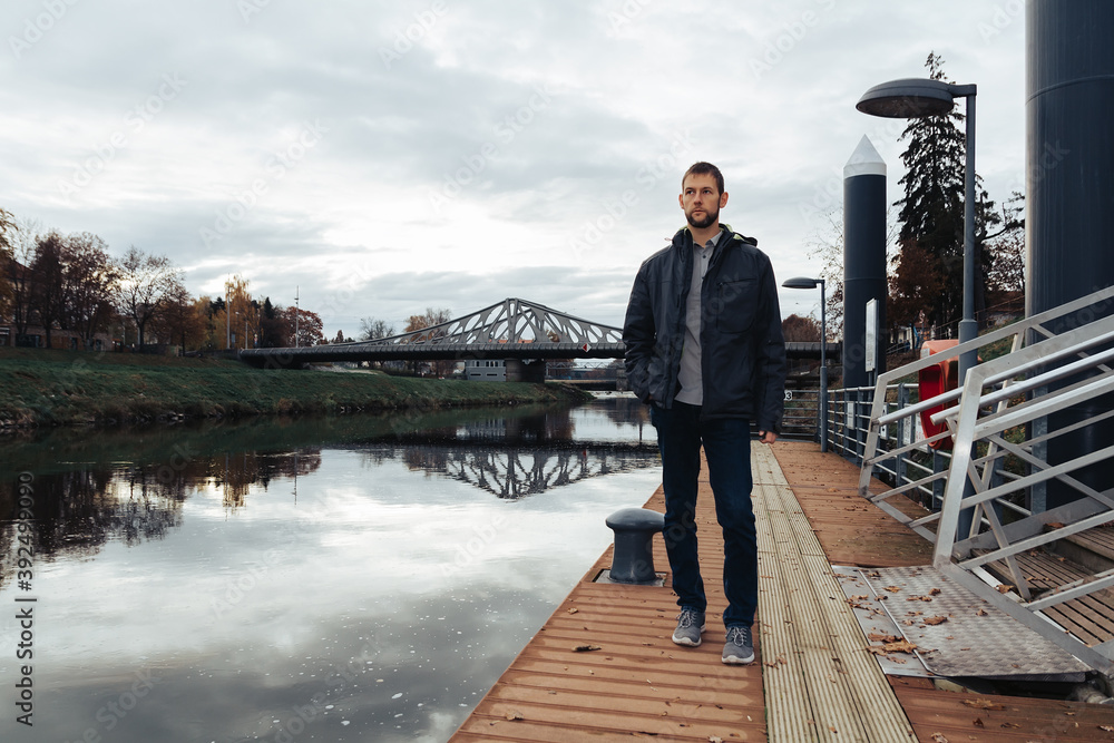 Portrait of young caucasian man in jacket walking on shipyard on Vltava river. Ceske Budejovice, Czech republic, toned photo