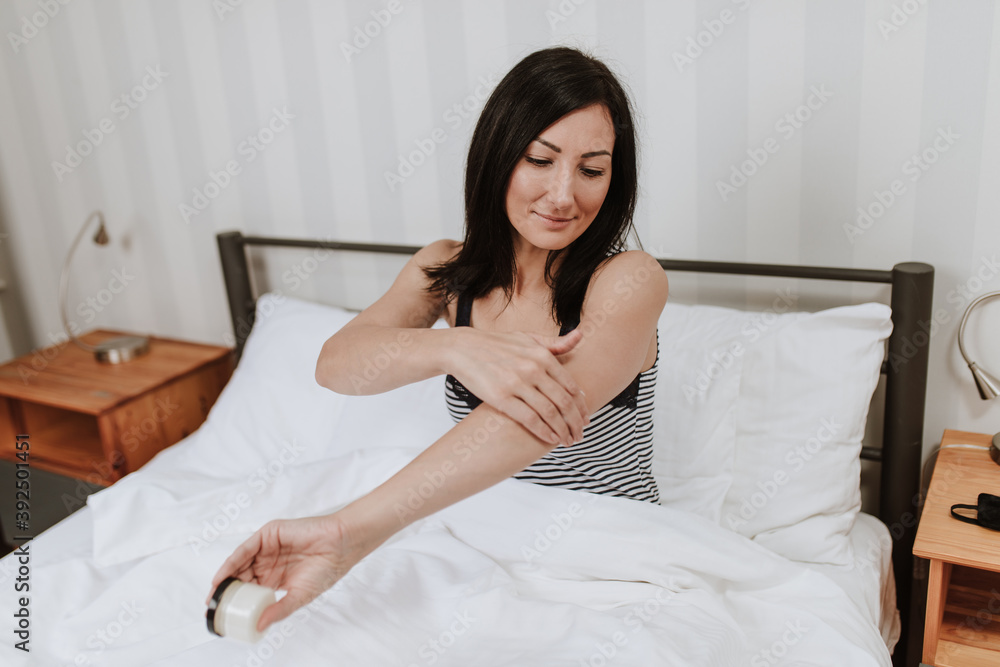 Attractive middle age woman lying in bedroom and using cosmetics skin cream as a daily evening routine before sleep. Skincare concept. Attractive middle age woman lying in bedroom and using cosmetics skin cream as a daily evening routine before sleep. Skincare concept.