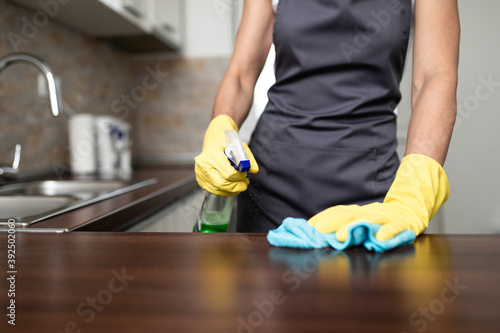 Beautiful and young housewife with protective gloves cleaning her modern apartment kitchen.