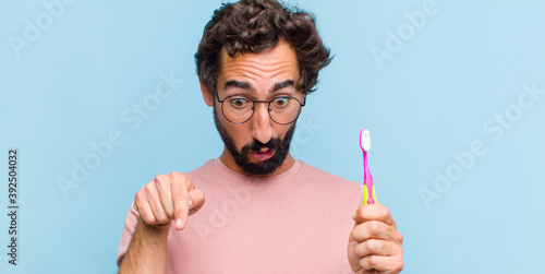 Fotografi young bearded man feeling shocked, open-mouthed and amazed, looking and pointing
