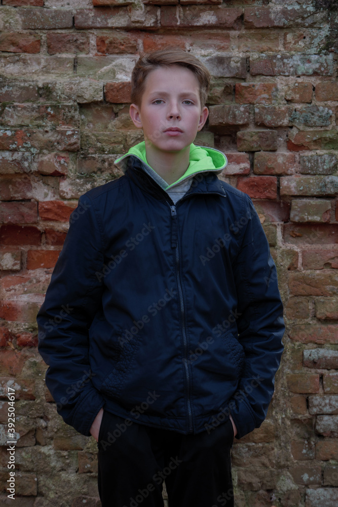 A 14 year old boy standing in front of an old brick wall. Boy standing