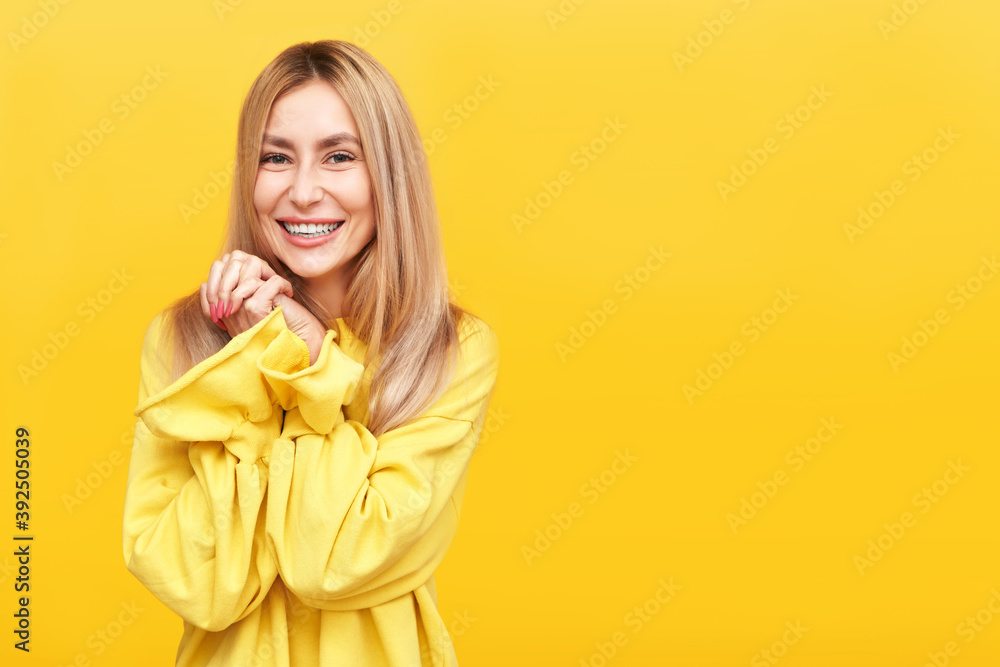Portrait upbeat pleasant looking glad young blonde woman in yellow smiling and looks into the camera with love, keeps hands together under chin, enjoying life isolated in studio Portrait upbeat pleasant looking glad young blonde woman in yellow smiling and looks into the camera with love, keeps hands together under chin, enjoying life isolated in studio