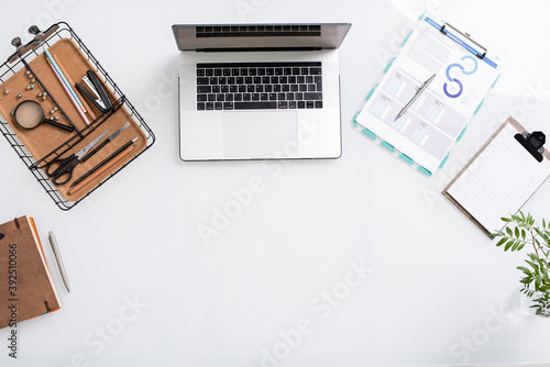 Top view of white copyspace surrounded by laptop, basket with office supplies