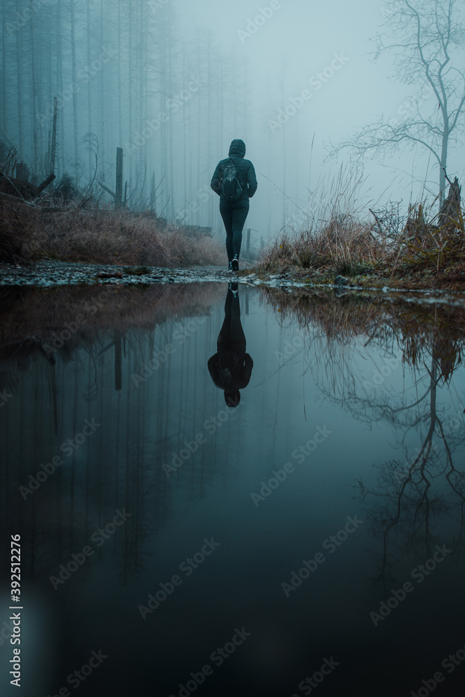 A reflection of the silhouette of a hiking girl on a rainy and foggy winter day in the mountains. Cold and moody outdoor adventure day. Harz National Park in Germany