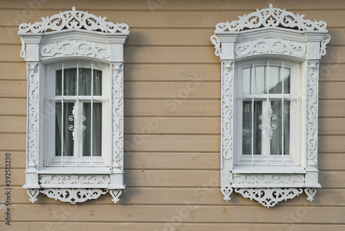 Two windows of an old wooden house in traditional folk russian style decorated with wood carving.