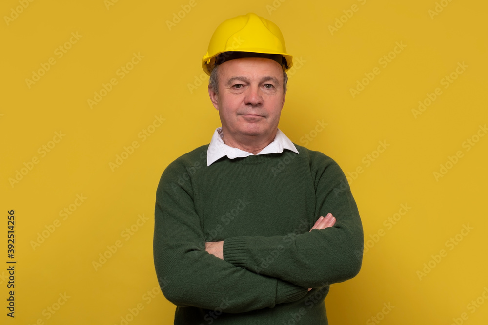 Senior foreman with special hard hat. Studio shot on yellow wall.