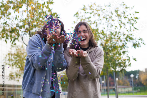 two young friends blowing confetti from hands. Friends celebrating outdoors