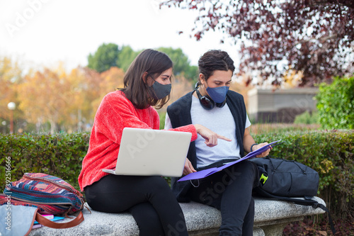 Two young students studying outdoor wearing mask during coronavirus times