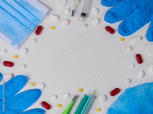 pills and gloves on white.Pills, mask, thermometer, syringes and gloves are arranged in a frame on a white background with a place for text in the middle, close-up top view.