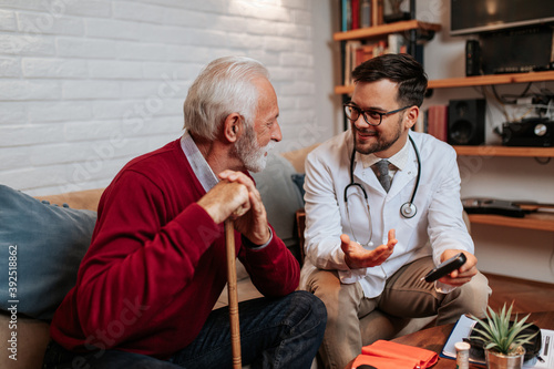 Young handsome doctor visiting examining his senior male patient at his home.