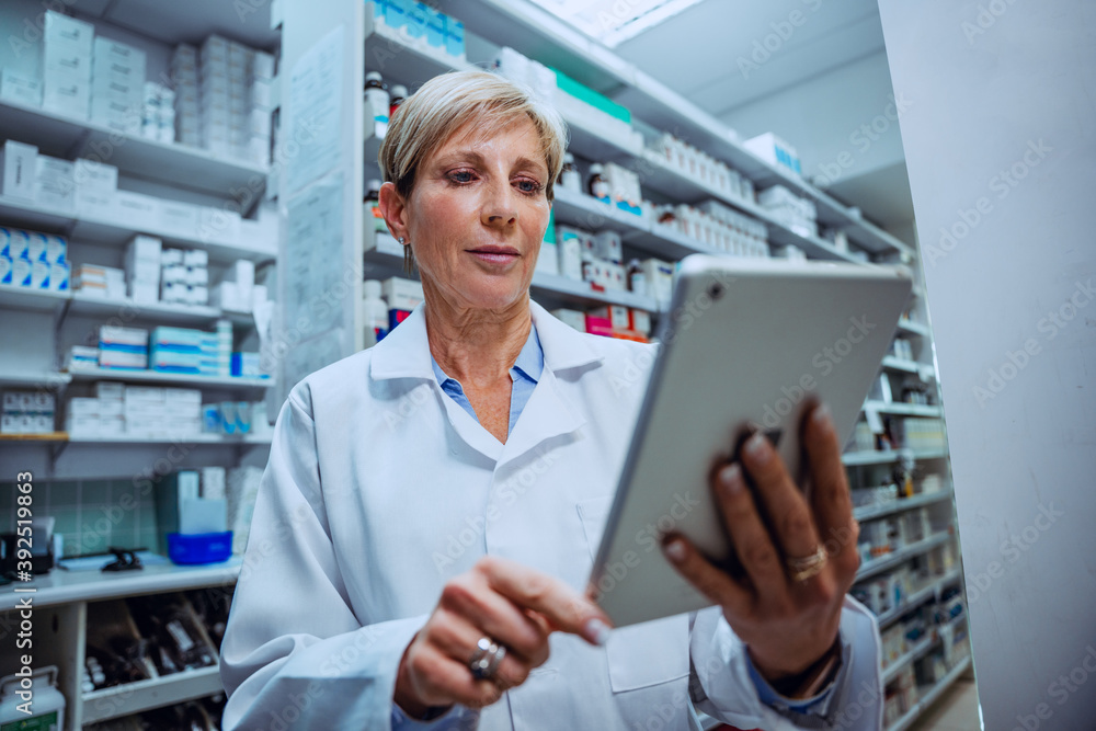 Caucasian senior pharmacist checking medication prescriptions on digital tablet standing in pharmacy 