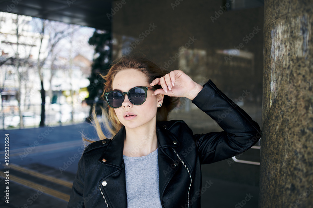 a woman stands under a bridge in the street wearing sunglasses and a leather jacket
