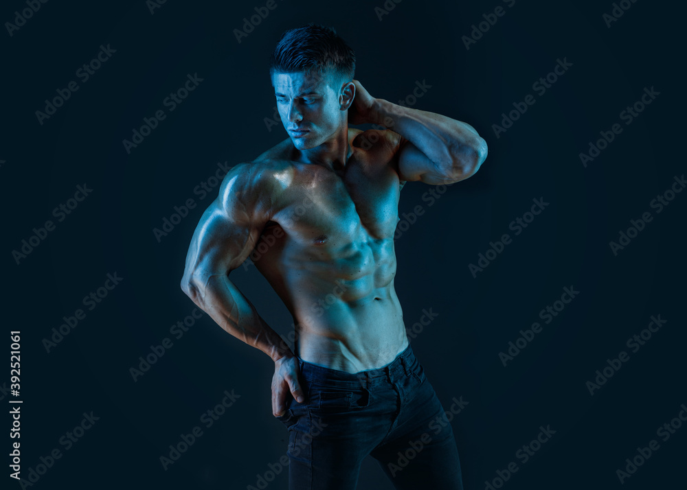 Muscular model sports young man on dark background. Fashion portrait of strong brutal guy. Sexy torso. Male flexing his muscles.