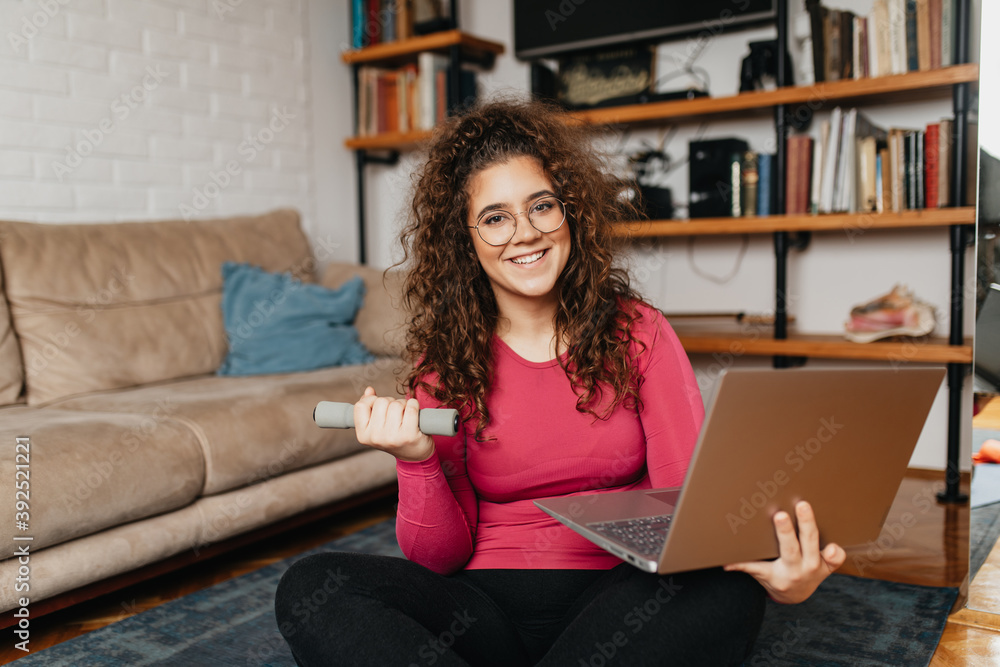 Young adult overweight girl exercising at home watching an instructor via laptop computer. Online fitness and pilates workout. Young adult overweight girl exercising at home watching an instructor via laptop computer. Online fitness and pilates workout.