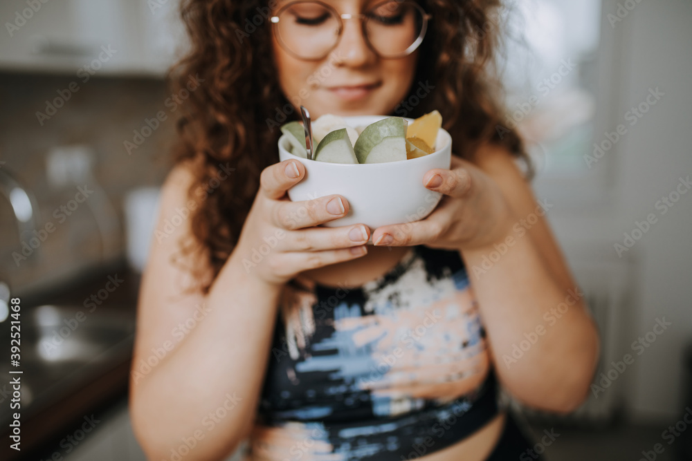Young overweight woman slicing fresh fruit and preparing healthy meal in home kitchen. Young overweight woman slicing fresh fruit and preparing healthy meal in home kitchen.