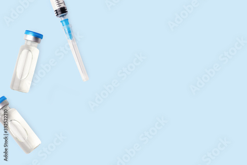 Two vaccine vial with blue caps and needle syringe. Vaccination concept. Disease injection rescue care treatment. Coronavirus medical bottle. Light blue background, copy space.
