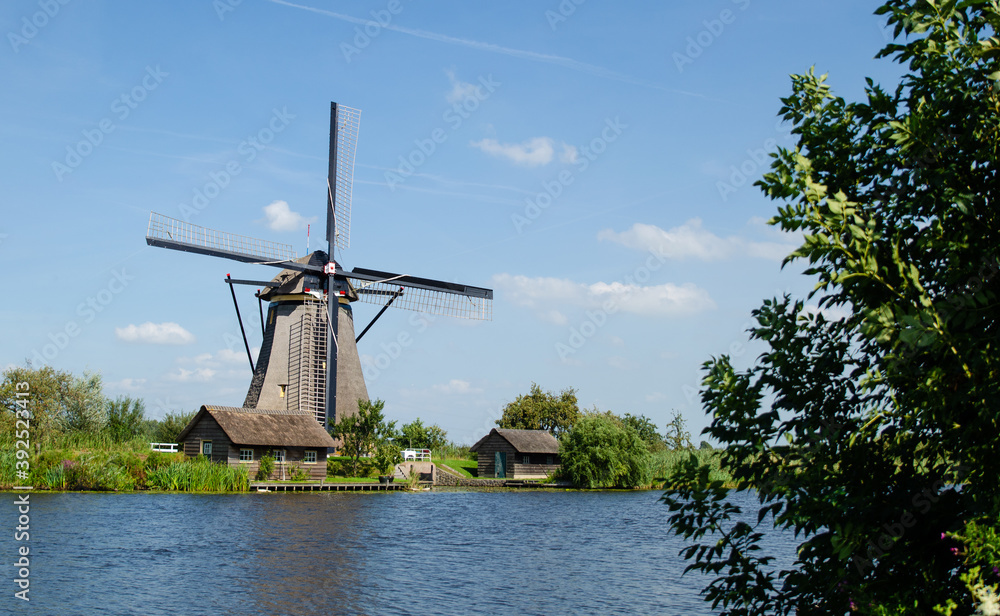 Kinderdijk, The Netherlands, August 2019. On a beautiful summer day a historic windmill, in perfect condition, in the Dutch countryside furrowed by canals lined with tall green grasses.