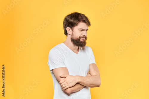 Bearded man in a white T-shirt gestures with his hands emotions studio yellow background