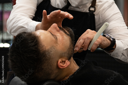 Barber with bow tie and white shirt shaving a customer