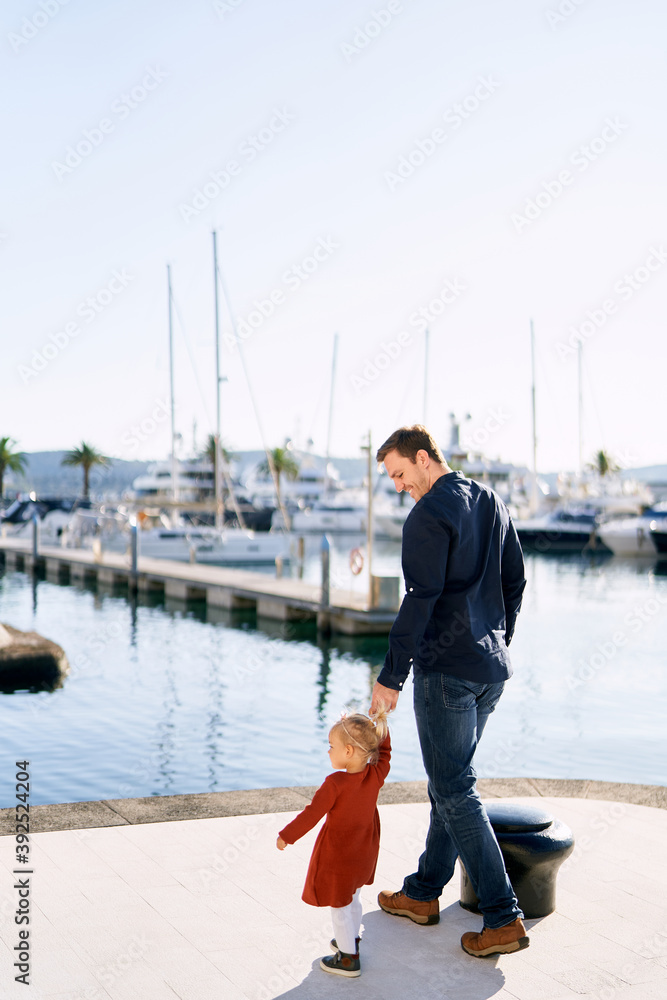 Man is walking hand in hand with his sweet 2-year old on a boat pier