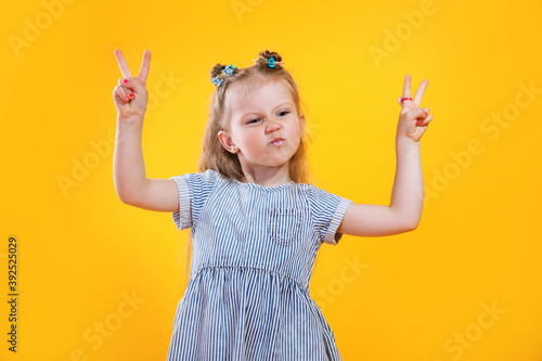 Funny little girl showing peace gesture on yellow background.. photo