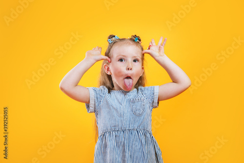Child girl making a face and showing her tongue on yellow background