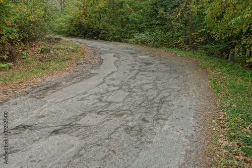 emergency section of the road from a turn with gray asphalt in cracks and potholes among green vegetation