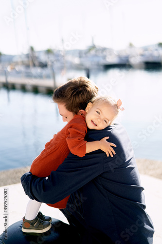 An adorable 2-year old girl is hugging her father at a boat marina