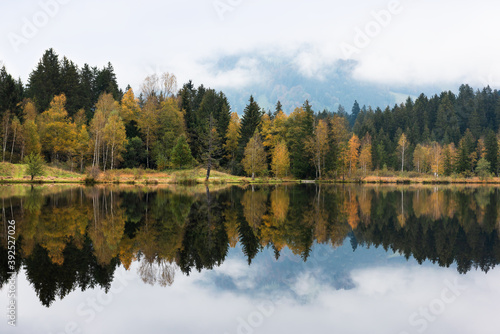 Beautiful view of idyllic colorful autumn scenery with reflecting in alpine mountain lake on a foggy day. Austria, Kitzbuhel.