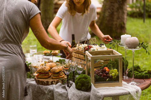 Anonymous female caterers setting up a table for a garden party with fresh organic, farm-to-table tapas