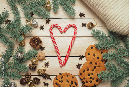 Christmas background with a knitted jacket with spruce branches, Christmas toys, cookies, heart-shaped candies in the center, with a nice warm soft light. Christmas background on wooden white boards