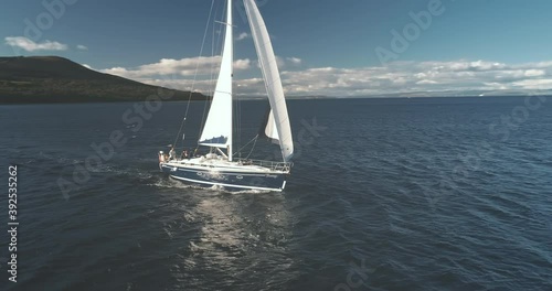 Slow motion sailboat race at ocean bay aerial. Summer cruise on luxury yacht. Passenger ship at sea shore of Arran island, Scotland, Europe. Sail boat at Brodick harbor. Cinematic seascape photo