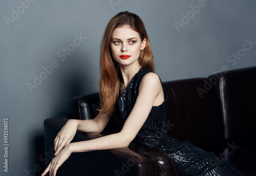 Elegant woman in a dark dress on a leather sofa and evening makeup © SHOTPRIME STUDIO