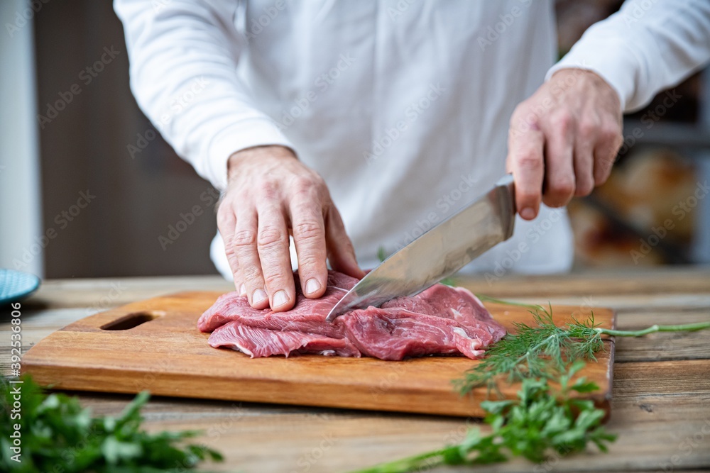Chef cuts a piece of beef on a wooden board in the kitchen.