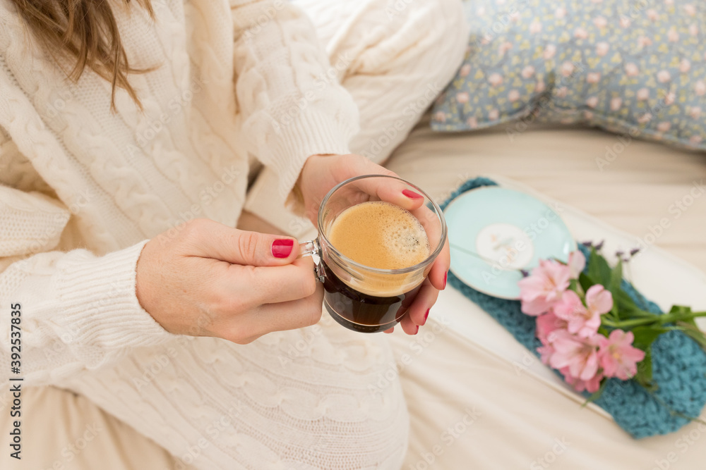 A foamy cup of coffee held by two red painted nails hands of a woman dressed on warm wool loungewear. A foamy cup of coffee held by two red painted nails hands of a woman dressed on warm wool loungewear.