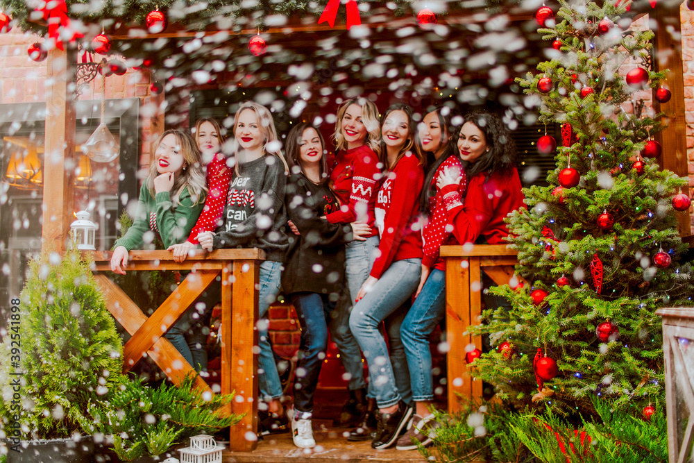 a group of beautiful women in Christmas sweaters pose under the flying snow