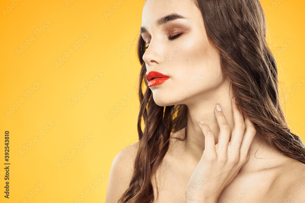 Beautiful brunette naked shoulders bright makeup red lips hairstyle close-up yellow background Beautiful brunette naked shoulders bright makeup red lips hairstyle close-up yellow background