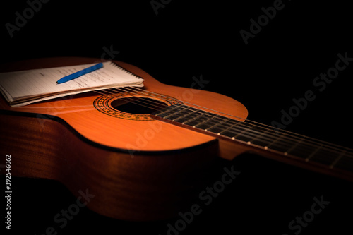 Acoustic guitar and note pad close up on black background. A studio shot with warm lighting, isolated. This image is ideal for songwriting concepts, lessons, music courses and teaching.