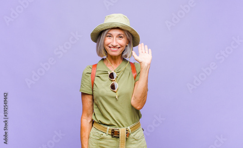 middle age woman smiling happily and cheerfully, waving hand, welcoming and greeting you, or saying goodbye photo