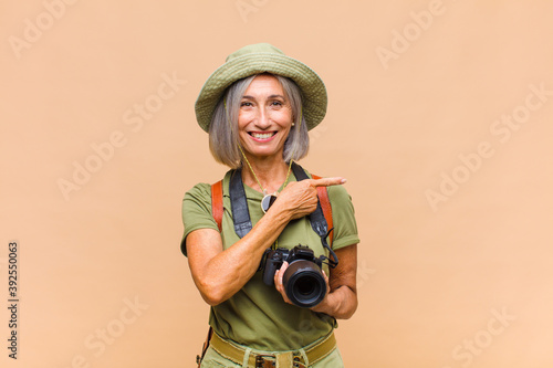 middle age woman smiling cheerfully, feeling happy and pointing to the side and upwards, showing object in copy space photo