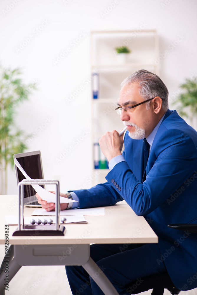 Old male employee businessman and meditation balls on the desk