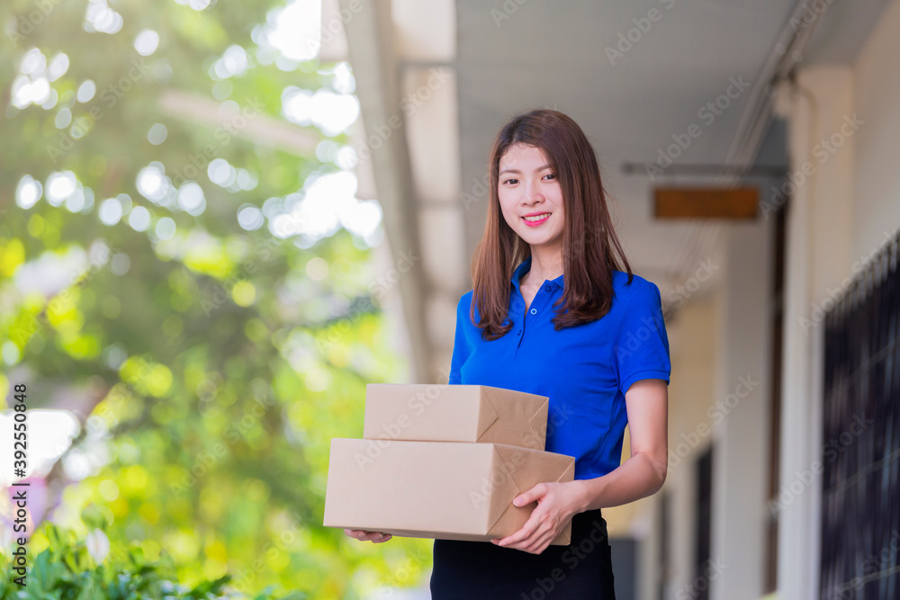 Fototapeta premium Advertising, Business, Transportation, Delivery Concept - The best delivery service. Beautiful Delivery asian woman holding pile of cardboard boxes in front while standing against residential house.