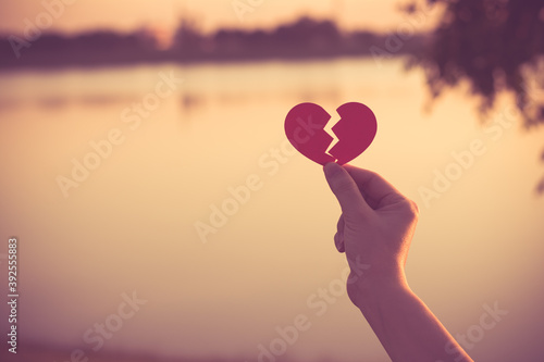 Silhouette broken heart, close up woman hand holding broken heart in the park.
