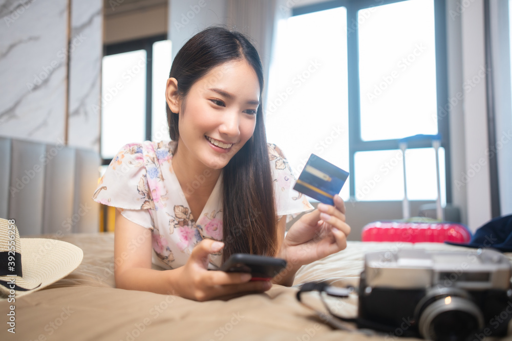 Asian beauty woman  plan for trip by mobile and credit card happily on the bed at home.