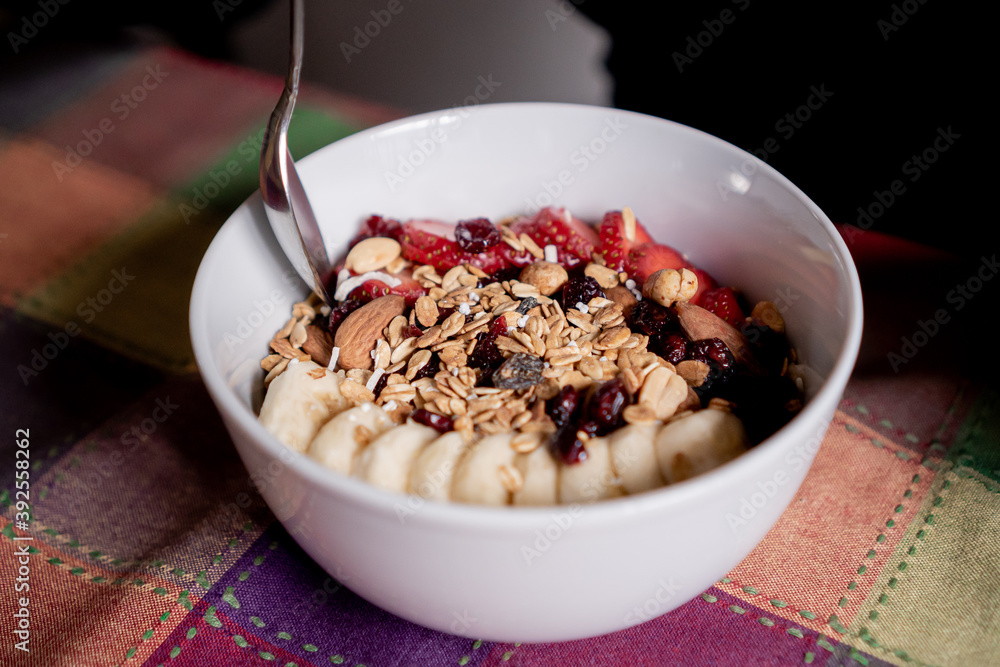 Delicious oatmeal with banana, strawberries, granola, blueberry, coconut and almonds on top with a spoon inside a white plate. Delicious oatmeal with banana, strawberries, granola, blueberry, coconut and almonds on top with a spoon inside a white plate.