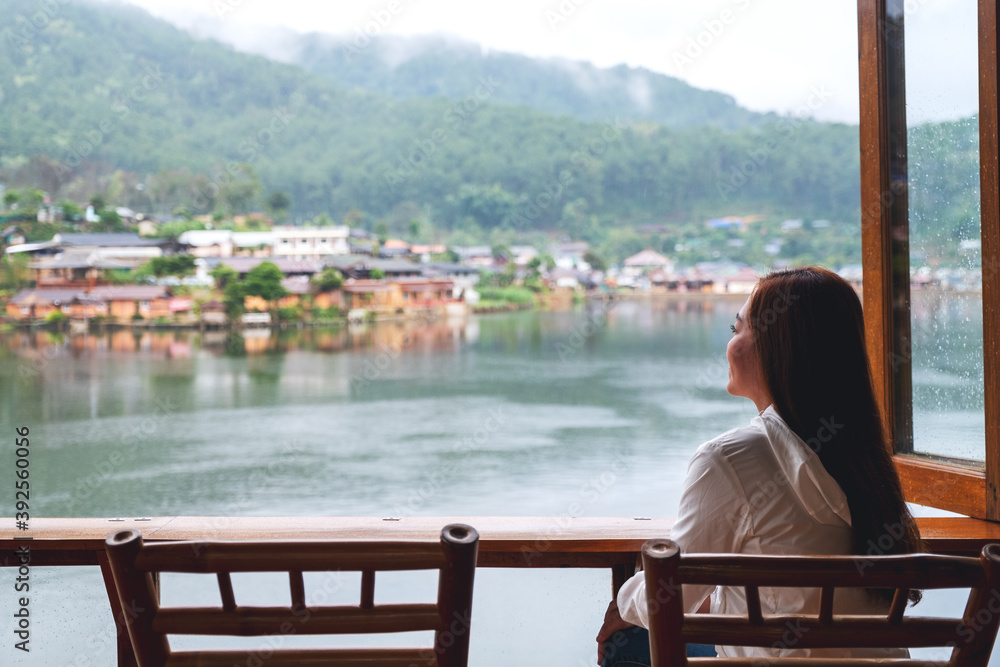 A young woman sitting on balcony and looking at a beautiful lake in mountains village A young woman sitting on balcony and looking at a beautiful lake in mountains village