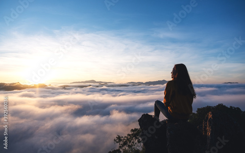 A female traveler sitting on the mountain peak, watching sunrise and sea of fog