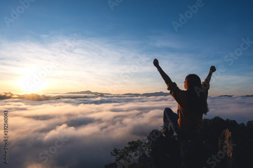 Foto A female traveler raising hands while sitting on the mountain peak, watching sun