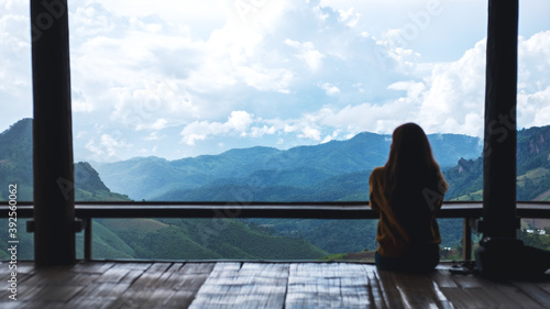 Rear view image of a female traveler sitting and looking at a beautiful mountain and nature view