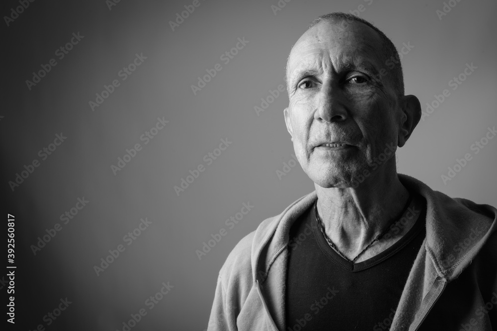 Close up of bald senior man thinking while wearing hoodie against gray background Close up of bald senior man thinking while wearing hoodie against gray background